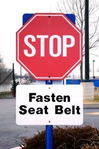 Photo of a Stop sign with another sign underneath that reads "Fasten Seat Belt"