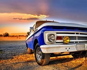 Close up of a blue pick up truck with a blue and orange sunset in the background