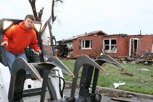 Sean Brady standing on his bobcat in front of the tornado damage