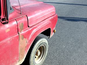 Close up of the hood of an old red pick up truck with rusted paint